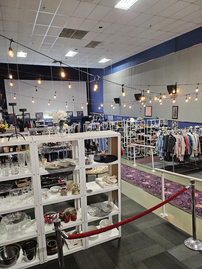Inside Alpha & Omega Outfitters — racks of clothing under string lights